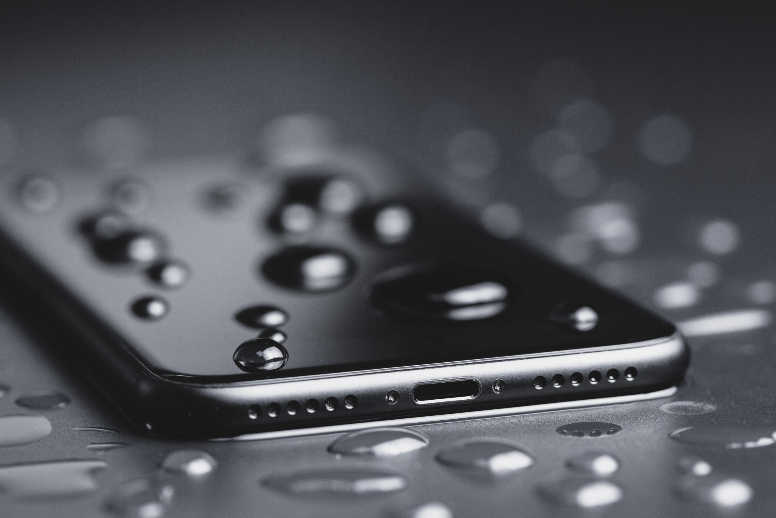 A smartphone with water droplets on top and around it.